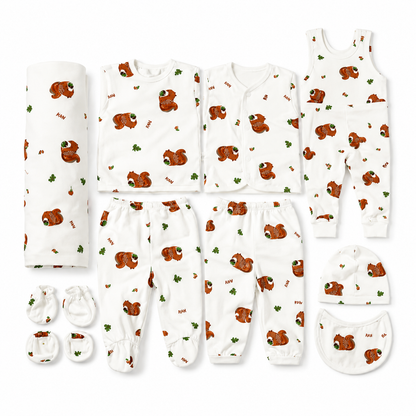 A baby clothing set laid out on a white background, including a rolled blanket, long-sleeve and short-sleeve tops, pants, a sleeveless jumpsuit, a beanie, mittens, and a bib. The set is white with a repeating brown bear and green leaf print.