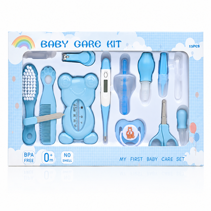 A baby care kit in its retail packaging, featuring various baby care tools such as a hairbrush, nail clipper, thermometer, pacifier clip, and nipple shield in light blue and white, with a rainbow graphic on a white and blue cloud-patterned box.