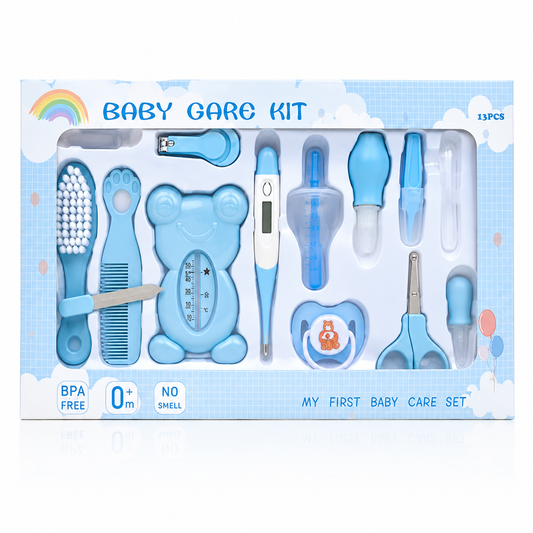 A baby care kit in its retail packaging, featuring various baby care tools such as a hairbrush, nail clipper, thermometer, pacifier clip, and nipple shield in light blue and white, with a rainbow graphic on a white and blue cloud-patterned box.