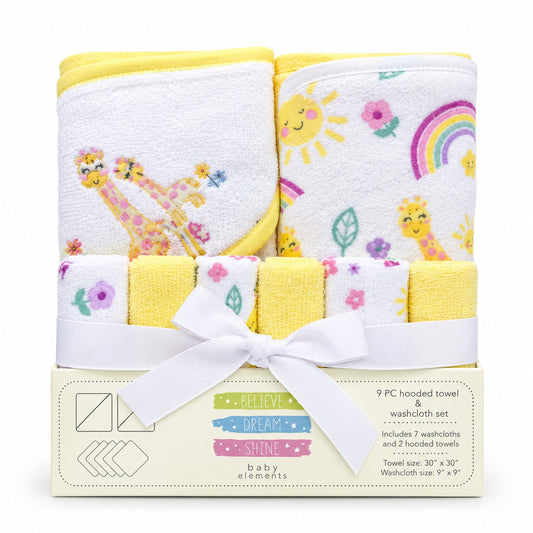 A 9-piece baby towel and washcloth set by Baby Elements, featuring yellow and white hooded towels with giraffes, a rainbow, and suns, tied with a white ribbon in its cream-colored packaging box.