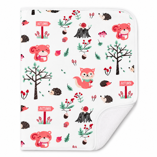 A square white Changing Sheett with a soft corner folded over to show the plush white underside. The front features an all-over autumn-themed pattern with pink bears, red foxes, hedgehogs, trees, berries, acorns, and 'AUTUMN' signs on a white background.