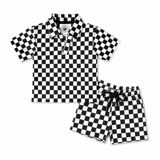 A two-piece baby clothing set featuring a short-sleeve polo shirt and matching shorts, both in a black and white checkerboard pattern. The polo shirt has a collar and a partial button placket, while the shorts have a matching black drawstring waist.