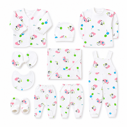 A baby clothing set laid out on a white background, including a long-sleeve top, footless onesie, pants, hat, bib, swaddle, and booties. The white garments are printed with a playful pattern of pink cartoon faces, green dots, and small black-and-white animal illustrations.