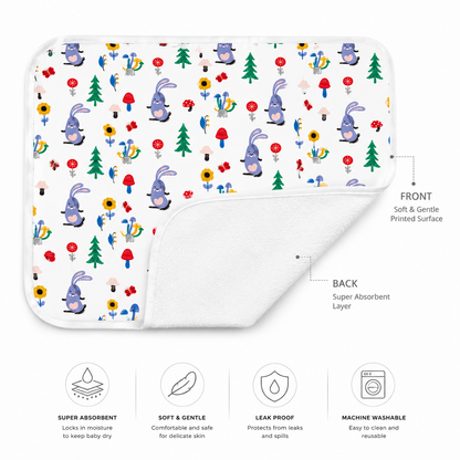 A baby changing mat shown on a white background with front and back views. The front side has a colorful printed pattern of cartoon bunnies, trees, flowers, and mushrooms.