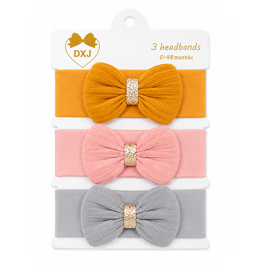 A 3-pack of DXJ brand baby headbands for 0-48 months, featuring a mustard yellow, light pink, and light gray fabric bow headband set with glittery gold center bands, displayed on a white cardboard hanger.