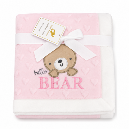 A folded baby blanket in light pink and white, featuring an embroidered brown bear face, pink 'BEAR' lettering, and a white ribbon with a paper tag tied around it, on a white background.