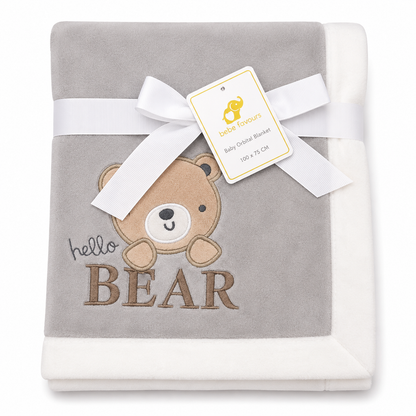 A folded baby blanket in light gray and white, featuring an embroidered brown teddy bear face and the words 'hello BEAR'. A white ribbon and a 'baby favourites' brand tag are tied around the center.