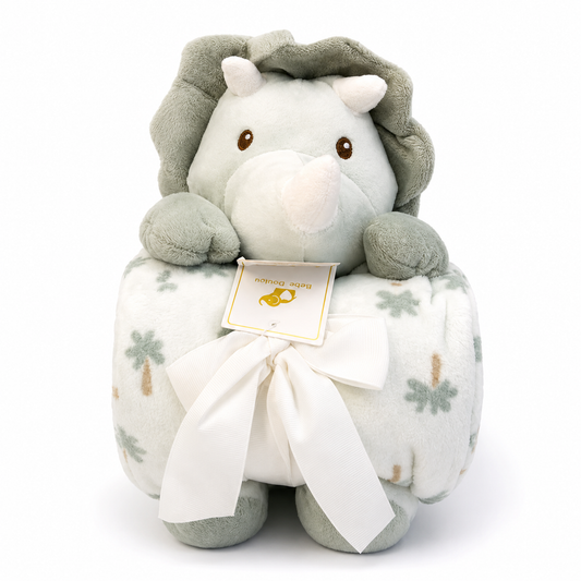 A plush rino toy sitting on a matching patterned blanket with a white ribbon bow. The lion is light gray with darker gray mane and ears, and the blanket has a white base with soft green and tan palm tree prints.