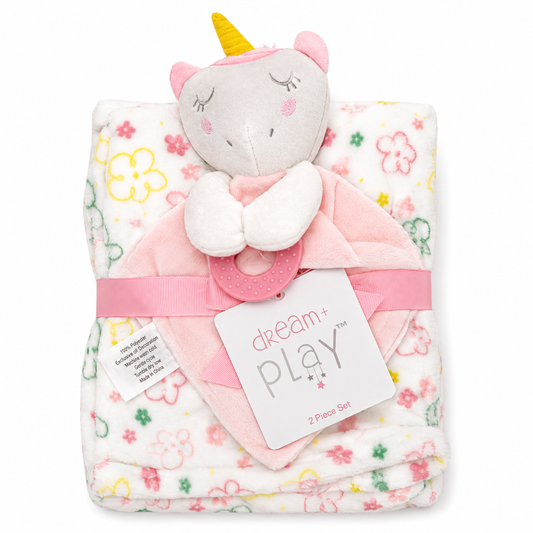 A baby comforter set featuring a folded white blanket with pink, yellow, and green floral patterns, a plush unicorn head topper with a yellow horn, a pink teething ring, and a pink ribbon with a 'dream play' tag.