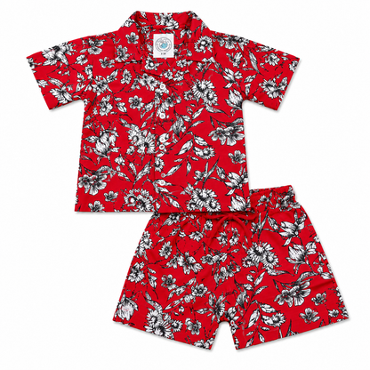 A two-piece kids' Hawaiian set featuring a short-sleeve button-up shirt and matching shorts, both in a vibrant red color with a black and white floral pattern, laid flat on a white background.