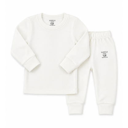 A two-piece baby loungewear set  featuring a long-sleeve crewneck top and matching jogger pants in off-white. The top has a small black printed brand logo on the inside neck, and the pants feature a small black logo on the left thigh.