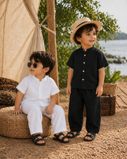 Two children in black and white outfits sitting outdoors near a tent with a scenic background.