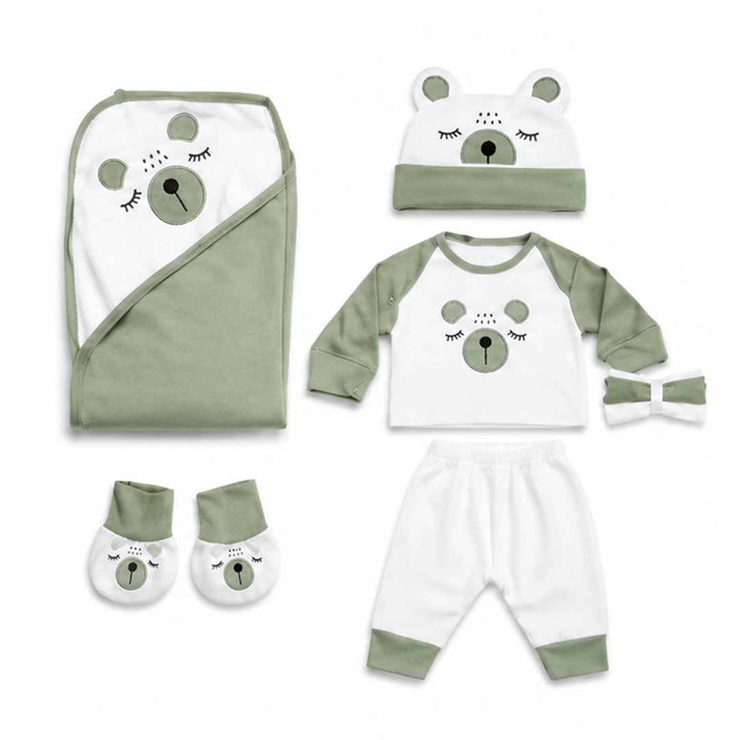 A baby clothing set laid out on a white background, including a swaddle wrap, long-sleeve top, pants, booties, hat, and headband, all in white and sage green with a bear face graphic.