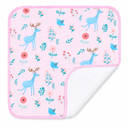 A square baby diaper changing sheet with a light pink background and a whimsical pattern of blue deer, birds, and floral elements, featuring a white fleece backing shown on the curled corner.