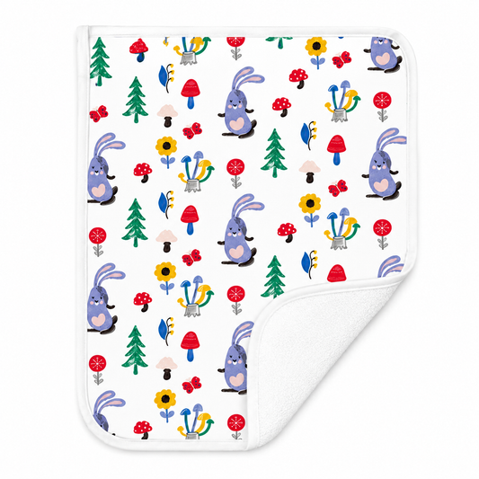 A square white diaper changing sheet with a colorful cartoon pattern of purple bunnies, red and pink mushrooms, green trees, and yellow flowers, shown on a white background with the corner folded over to reveal the white reverse side.