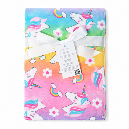 A folded plush blanket featuring a colorful unicorn print, wrapped with a white ribbon and a product tag, shown against a plain white background.