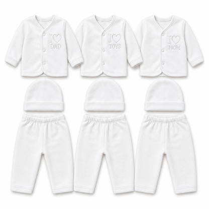 Six white baby clothing sets arranged in two rows on a plain white background. The top row shows long-sleeve button-front cardigans with embroidered text reading 'I [heart] DAD', 'I [heart] TOYS', and 'I [heart] MOM', paired with matching beanies.