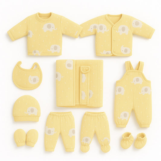 A baby clothing set laid out on a white background, including a long-sleeve shirt, cardigan, bib, hat, footed pants, overalls, booties, and a folded blanket. The items are pale yellow with a soft elephant print.